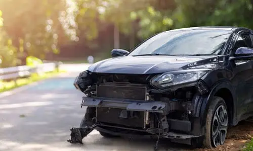 سيارة سيدان سوداء متضررة بالكامل على جانب طريق فرعي بعد حادث خطير