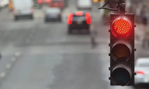 لقطة مقرّبة لإشارة مرور حمراء مع حركة مرور غير واضحة في الخلفية