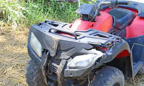 مركبة ATV حمراء مع تلف في المصباح الأمامي الأيسر والهيكل، في منتصف طريق وعر بعد وقوع حادث.
