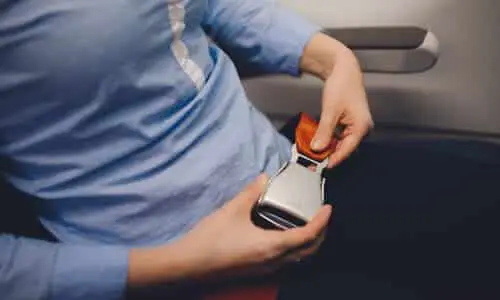 لقطة مقرّبة لجزء علوي من جسد امرأة ترتدي بلوزة زرقاء وهي تربط حزام الأمان داخل طائرة.