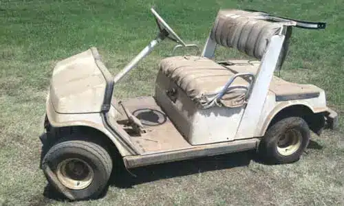 عربة جولف بيضاء متربة مع إطار أمامي أيسر مفرغ من الهواء، متوقفة على عشب ملعب جولف.