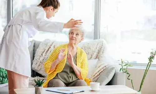 مقدمة رعاية تصرخ على امرأة مسنّة جالسة على أريكة داخل دار رعاية مسنين.