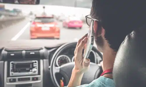 سائق يستخدم الهاتف أثناء القيادة وسط الازدحام، لتمثيل مخاطر القيادة المشتّتة والحاجة إلى دعم قانوني بعد الحادث.