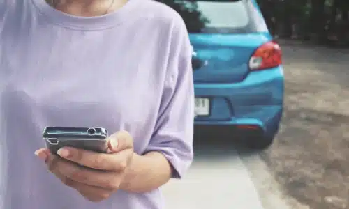 امرأة تستخدم هاتفها قرب سيارة زرقاء متوقفة، لتمثيل موقف يناسب قضايا حوادث النقل التشاركي في سافانا.