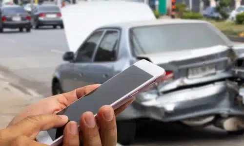 شخص يستخدم هاتفًا وخلفه سيارة متعرّضة لحادث، لتمثيل قضايا حوادث Uber في سافانا.