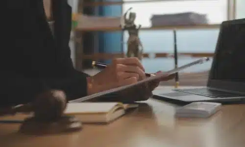 محامٍ يراجع مستندات على مكتب، وبجواره مطرقة القضاء وتمثال سيدة العدالة وجهاز حاسوب محمول، في إشارة إلى تمثيل قانوني في قضية حادث قارب.