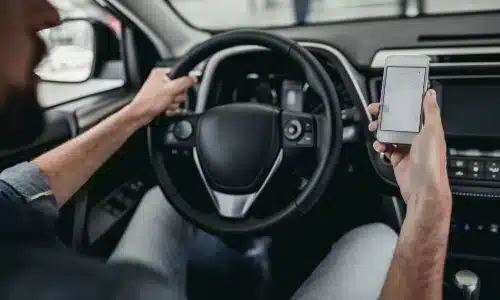 رجل يقود سيارة بينما يمسك هاتفًا ذكيًا يعرض خريطة ملاحة، في تصوير لحادث ناتج عن قيادة مشتتة.