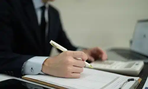 محامي حوادث الدراجات النارية في غينزفيل يكتب على مكتبه بينما يستخدم آلة حاسبة بيده الأخرى لحساب التكاليف.