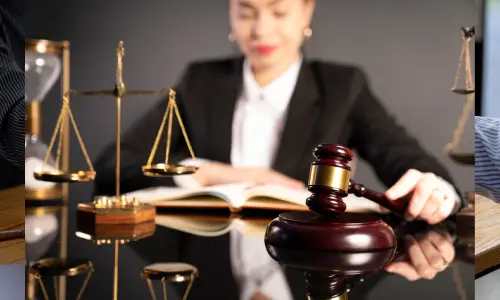 محامية تجلس خلف مكتبها تمسك بالمطرقة فوق قاعدة الطرق وتراجع كتابًا قانونيًا للاستناد إليه.