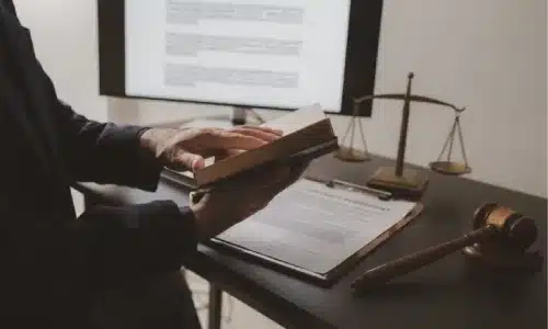 محامٍ يجلس على مكتب ويقلب صفحات كتاب قانون مفتوح استعدادًا لقضية.
