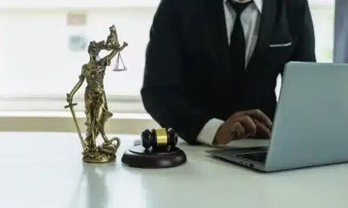 محامٍ مختص بقضايا الإصابات الشخصية يكتب على حاسوب محمول بجوار تمثال سيدة العدالة على المكتب.
