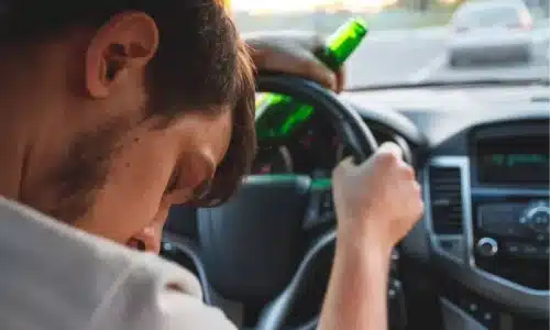 سائق مخمور نائم خلف عجلة القيادة ممسكًا بزجاجة في وسط حركة المرور.