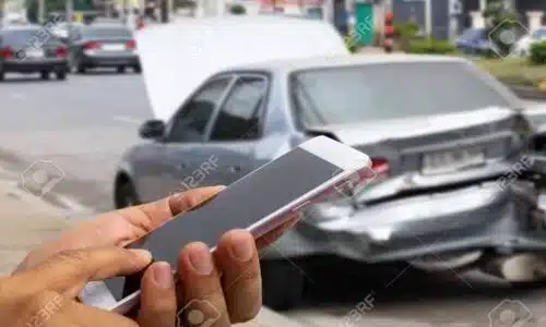 لقطة مقرّبة لرجل يحمل هاتفًا ويعرض صورة حادث سيارة.
