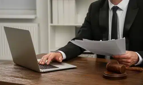محامي مسؤولية الأماكن يكتب على حاسوب محمول بينما يحمل ملفات بيده اليسرى داخل مكتب محاماة في هيوستن.