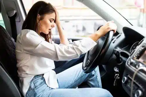 سيدة تبدو متأثرة داخل سيارتها بعد حادث مع سائق غير كافي التأمين.