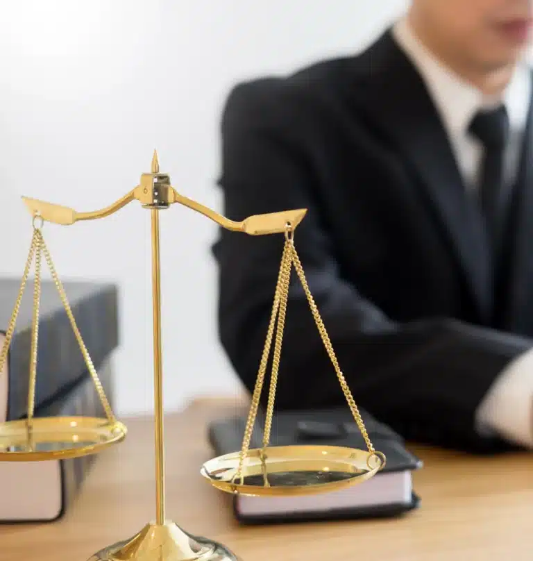 محامٍ يجلس على مكتبه مع ميزان العدالة داخل مكتب قانوني لتقديم استشارة قانونية احترافية