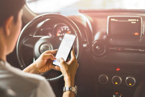 Un primer plano de la mano de una mujer sosteniendo un teléfono celular mientras envía mensajes de texto y conduce.