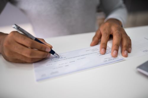 Un primer plano de la mano de un hombre escribiendo un cheque de liquidación.