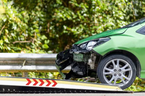 Un coche verde con el frontal destrozado atropellando a un camión después de que un accidente lo destrozara.