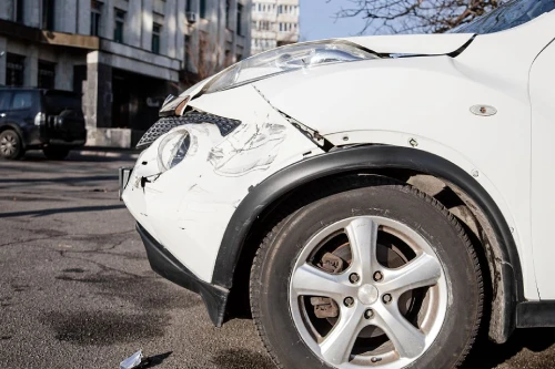 La parte delantera de un automóvil blanco rayada y abollada después de un accidente a baja velocidad en una carretera de la ciudad.