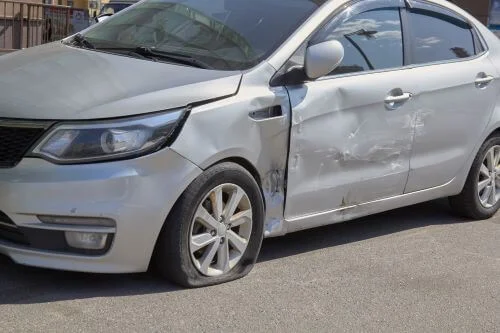 Un automóvil gris con daños en la puerta del conductor después de un accidente de atropello y fuga.
