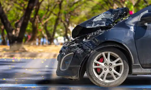 Un sedán azul oscuro con la parte frontal destrozado en una carretera suburbana.