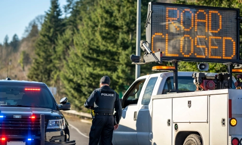 Un oficial policial y su vehículo al lado de una señal LED de calle cerrada en la escena de un accidente.
