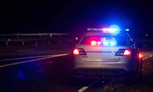 Una captura por detrás de un auto policial detenido al lado de la calle de noche.