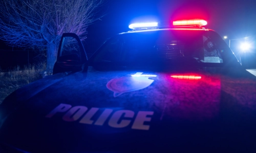 Una captura de cerca de un vehículo policial con una puerta abierta y luces prendidas en la escena de un accidente.