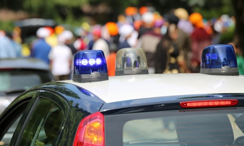 Una captura de cerca del techo de un auto policial con una multitud de gente concentrada en el fondo.