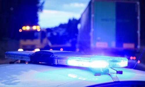 Las luces de un auto policial que está estacionado detrás de unos camiones grandes involucrados en un accidente.