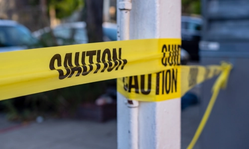 Cinta amarilla en la escena de un accidente con los oficiales policiales respondiendo en el fondo.