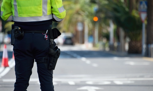 Un oficial de policía caminando junto a una fila de conos de tráfico en una calle de la ciudad durante el día.