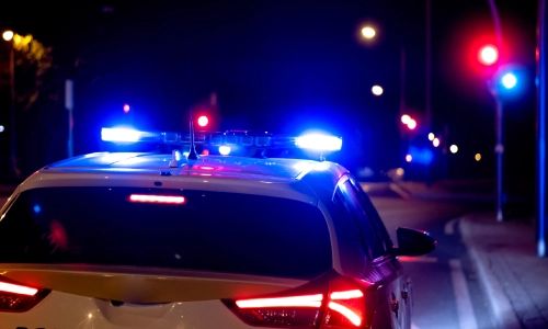 Un coche de policía parando al lado de la carretera por la noche con sus luces de emergencia encendidas.