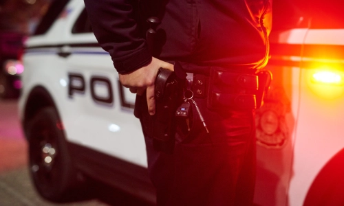 Un oficial de policía apoyado en su coche con una mano en su funda.