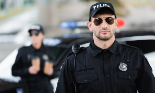 Oficiales de policía con gafas de sol de pie junto a su vehículo por la tarde.