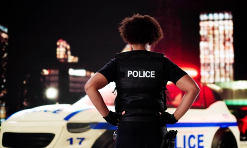 Una oficial de policía de pie con las manos en las caderas mientras mira su vehículo.