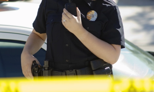 Un oficial de policía con una mano en su funda y la otra sosteniendo su radio.