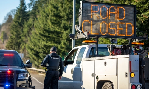 El coche de un oficial de policía detenido junto a un camión con una señal LED de carretera cerrada advirtiendo sobre un accidente.