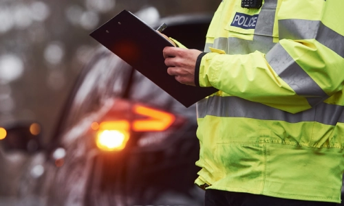 Un oficial de policía sosteniendo un portapapeles y documentando un accidente en un día lluvioso.