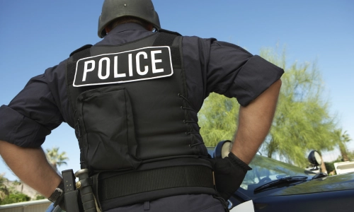 Una toma baja de un oficial de policía con las manos en la cintura mientras está de pie frente a su vehículo.