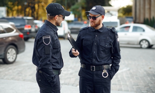 Dos oficiales de policía hablando con uno de ellos sosteniendo un portapapeles bajo el brazo.