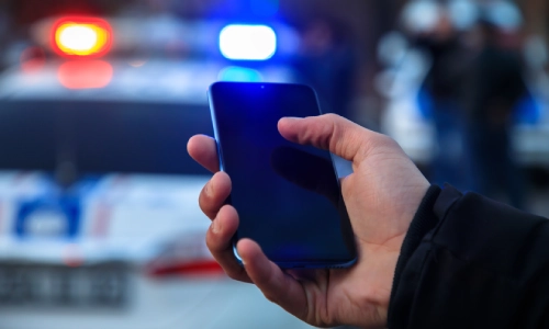 Una toma en primera persona de una víctima de accidente sosteniendo un teléfono con un vehículo policial al fondo.