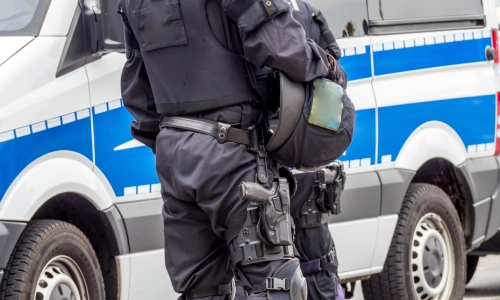 Un oficial de policía sosteniendo su casco a la altura de la cintura y de pie junto a su vehículo.