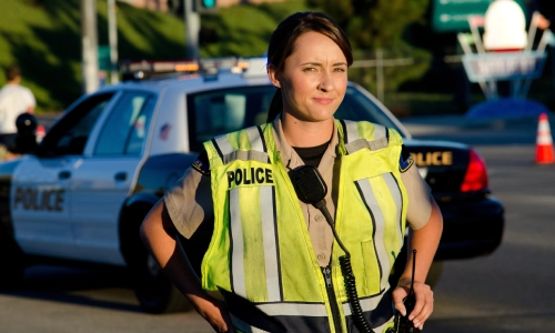 Un oficial policial sonriendo con manos en sus caderas mientras ve hacia la cámara.