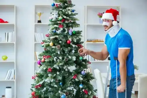 An injured man stands next to a christmas tree.