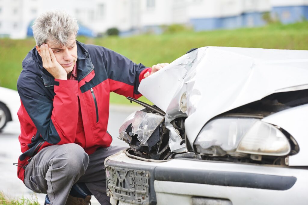 Upset man kneels beside his crashed vehicle after accident with an uninsured motorist.