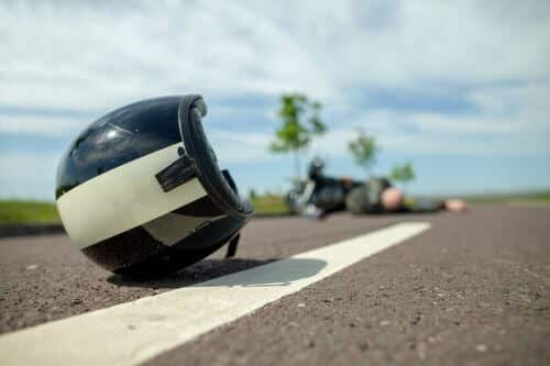 A man with common motorcycle injuries lays in the road next to his helmet that has fallen off