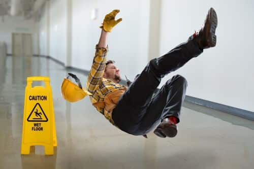 A man slips and falls in the workplace next to a sign meant to prevent slipping