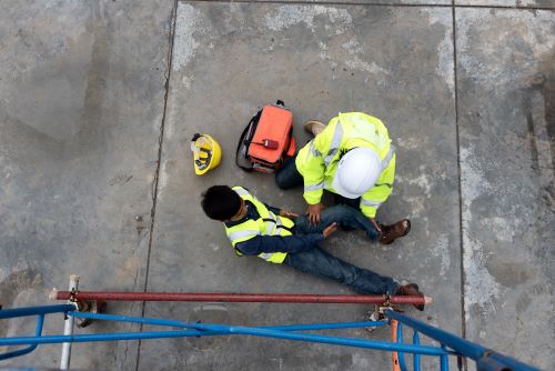 An injured construction worker is cared for by another employee after falling from a substantial height.